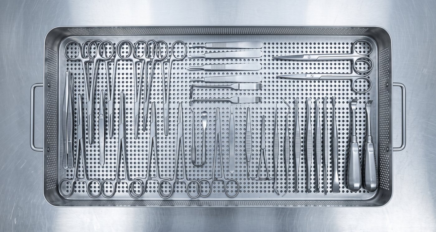 Stainless surgical instruments laid out in a perforated stainless reprocessing tray