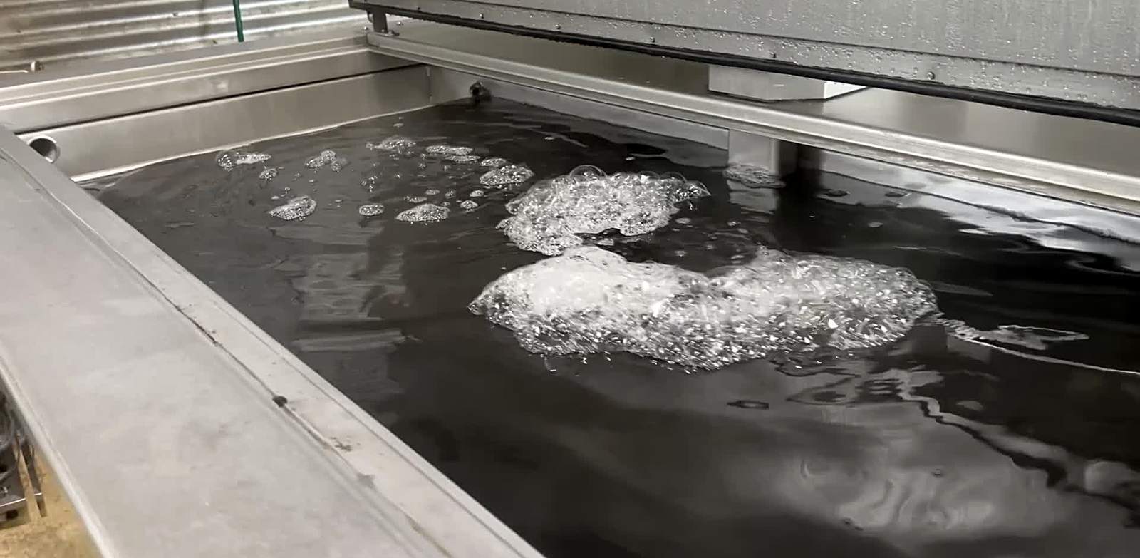 Cavitation rolling the surface of a dark working ultrasonic bath — the chemistry doing the cleaning