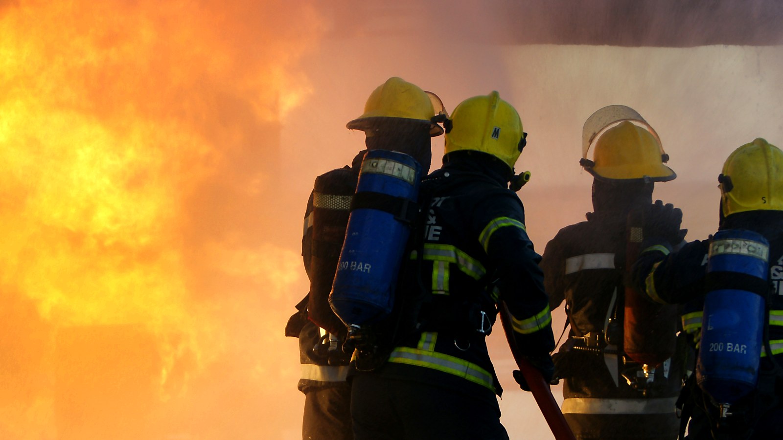 Firefighters in breathing apparatus facing a wall of flame