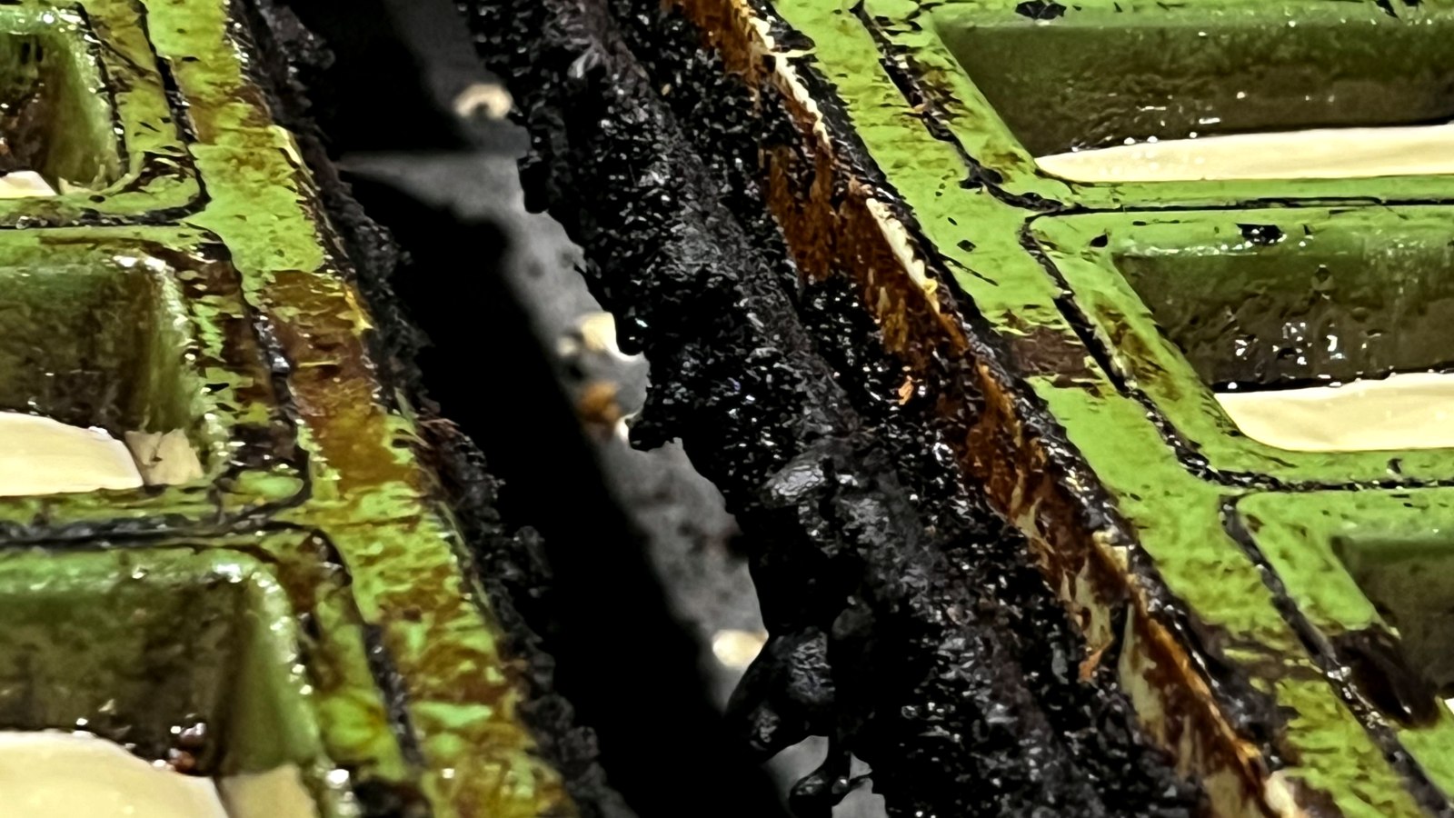 Carbonised product build-up between baking mould trays — before cleaning