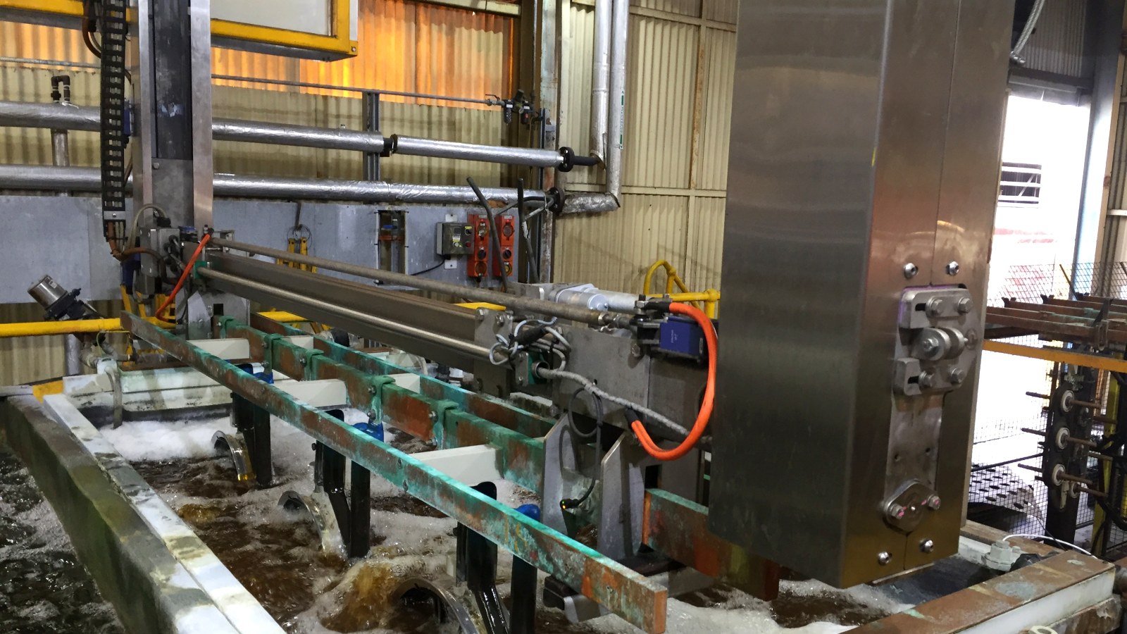 Plating line transporter lowering a rack of parts into a process tank