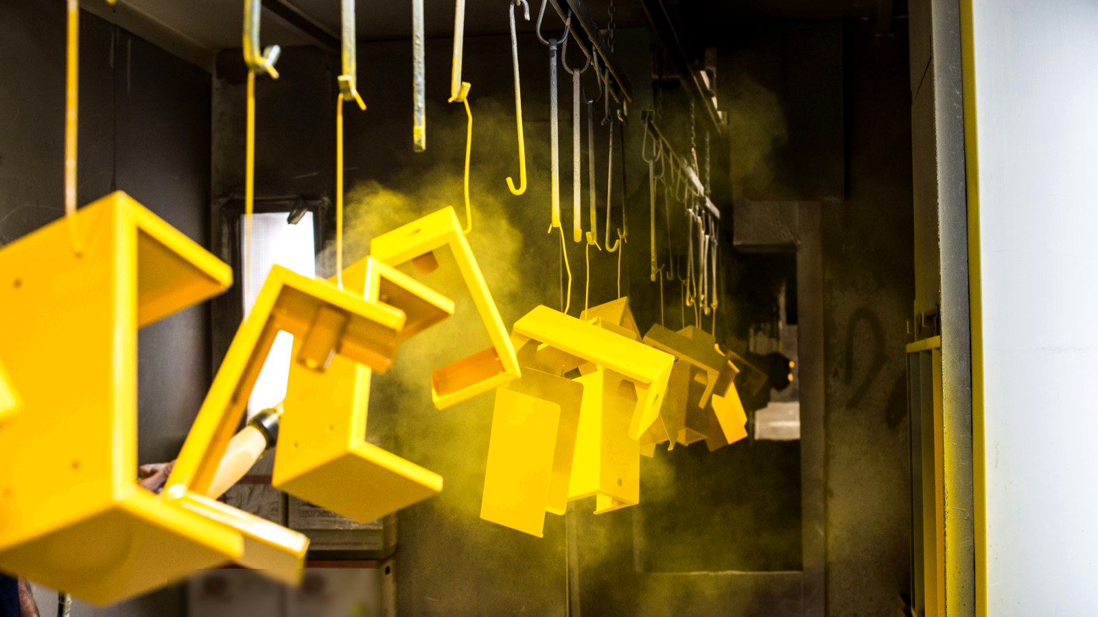 Powder coating booth — parts on hangers in a cloud of yellow powder