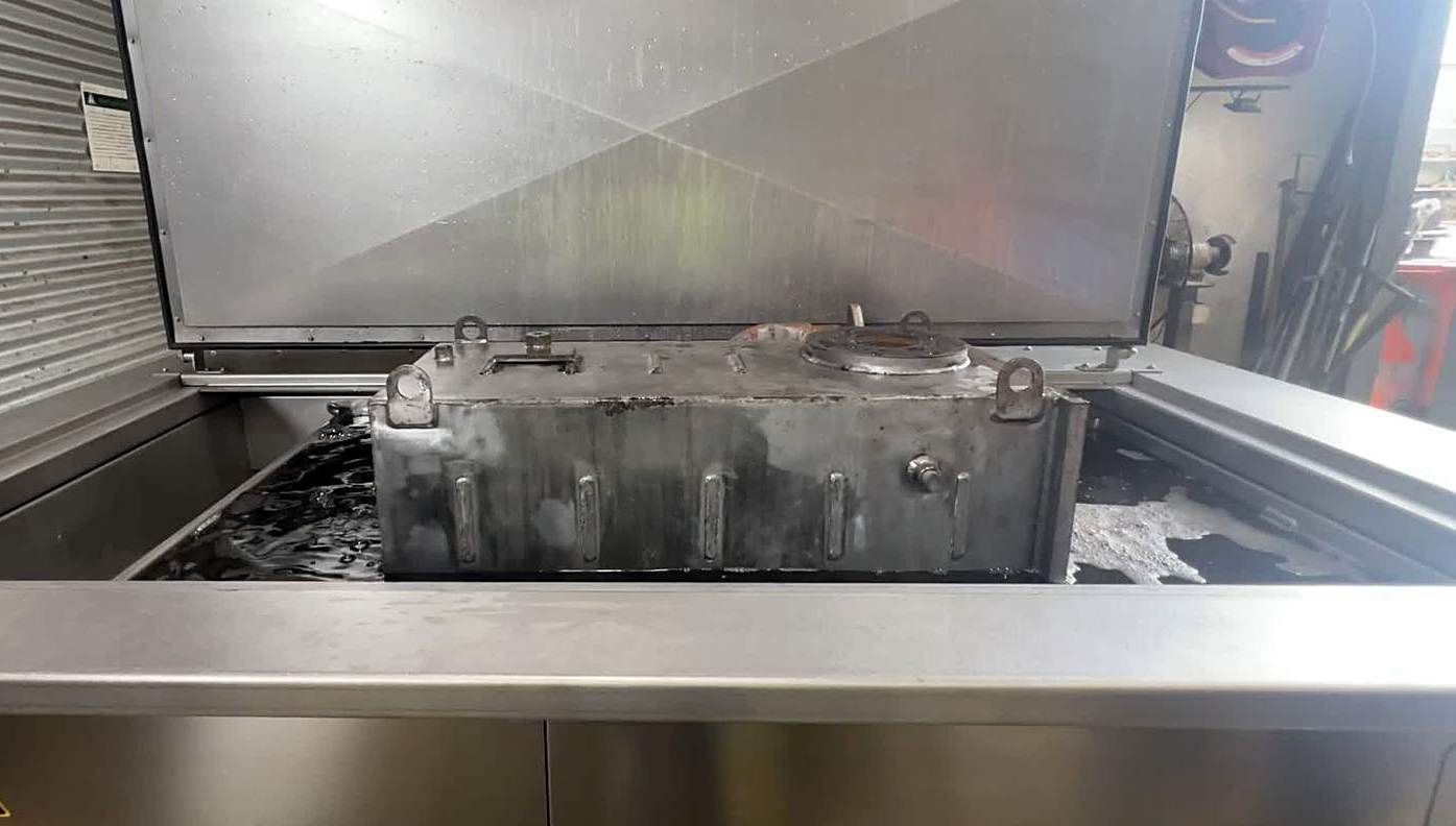 A soiled gearbox casting sitting in a working ultrasonic bath with the lid open — every one of the seven factors in play