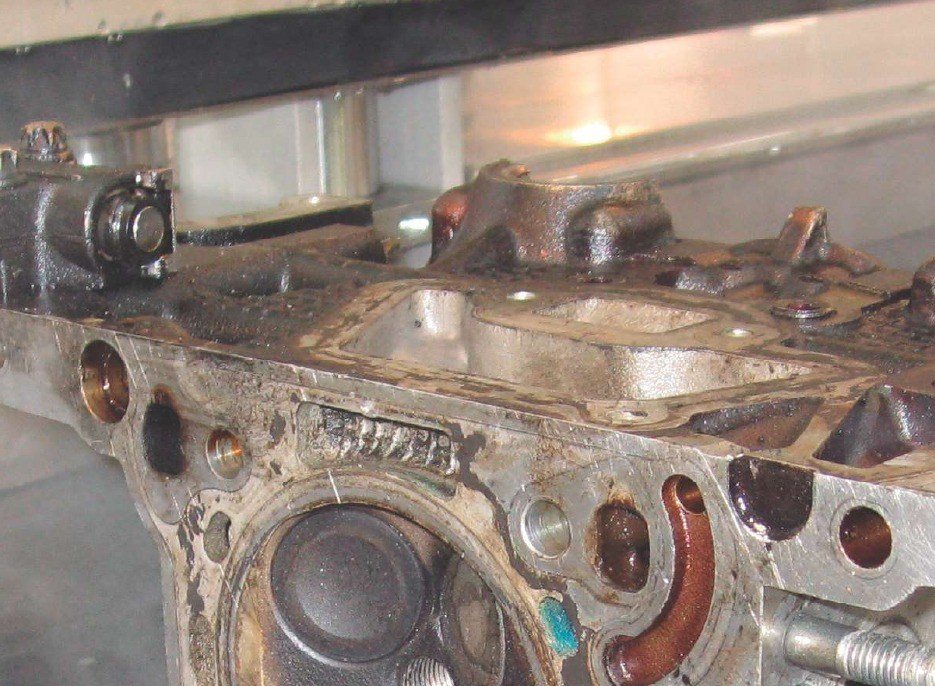 A cylinder head heavily coated in carbon and oil sitting in an ultrasonic cleaning tank